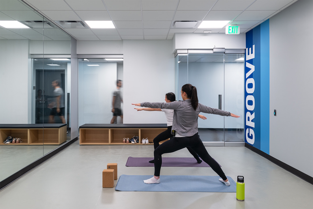 Two young women doing a yoga pose in an exercise room. The word Groove is edged on the wall.