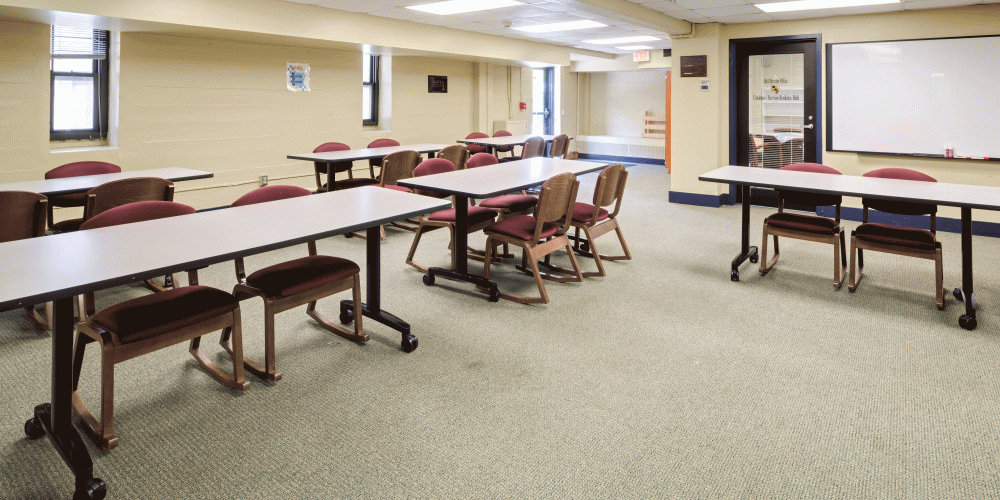Activity room with a screen, long tables and chairs.