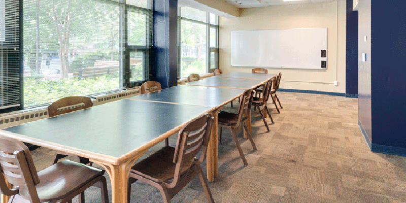 Meeting room with table, chairs, and a white board. One side of the wall is made up of glass pane windows.