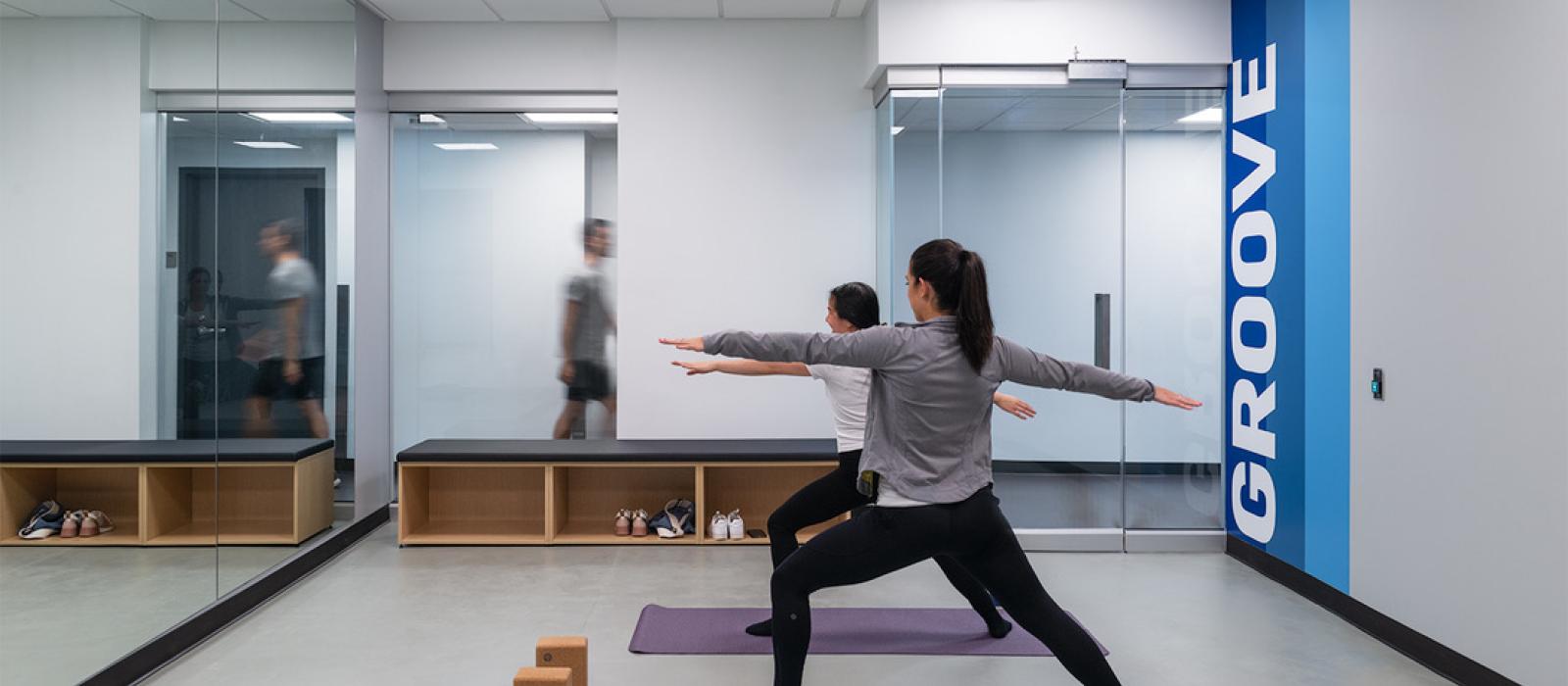 Two young women doing a yoga pose in an exercise room. The word Groove is edged on the wall.
