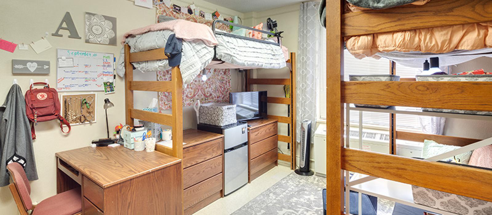 Bedroom with a high bed with appliances and drawers underneath it, a bunk bed, and a desk with a chair..
